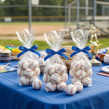 White chocolate baseballs with red stitching packed in clear cellophane party favor bags tied with blue ribbon on a ballfield party table