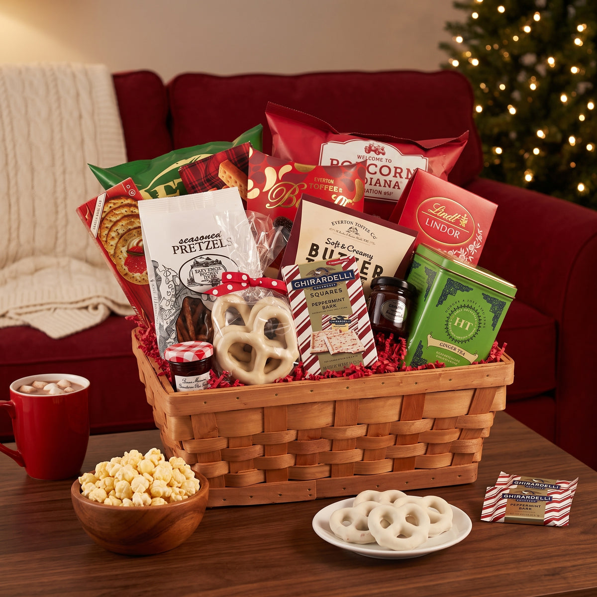 Holiday cheer Christmas gift basket in willow with chips, pretzels, shortbread, chocolates and a tea tin, opened on a family room coffee table on movie night