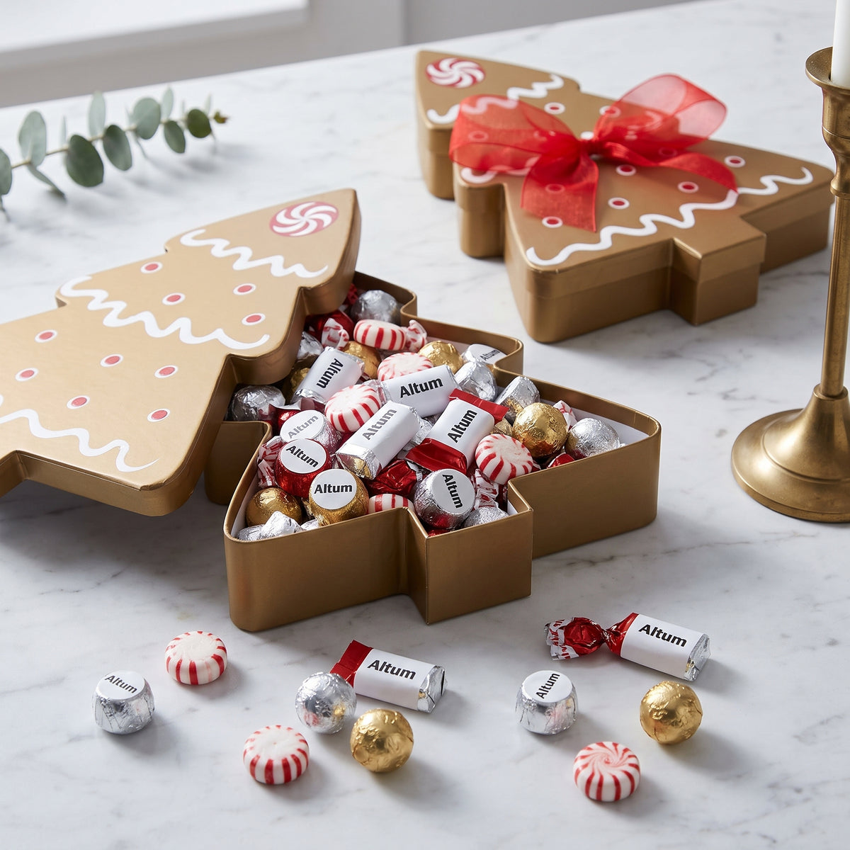 Holiday tree candy box shaped like an iced gingerbread tree, open and filled with wrapped chocolates and peppermints on white marble