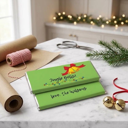 Jingle Bells wrapped Hershey's chocolate bars on a marble kitchen island beside kraft wrapping paper, twine, and brass sleigh bells
