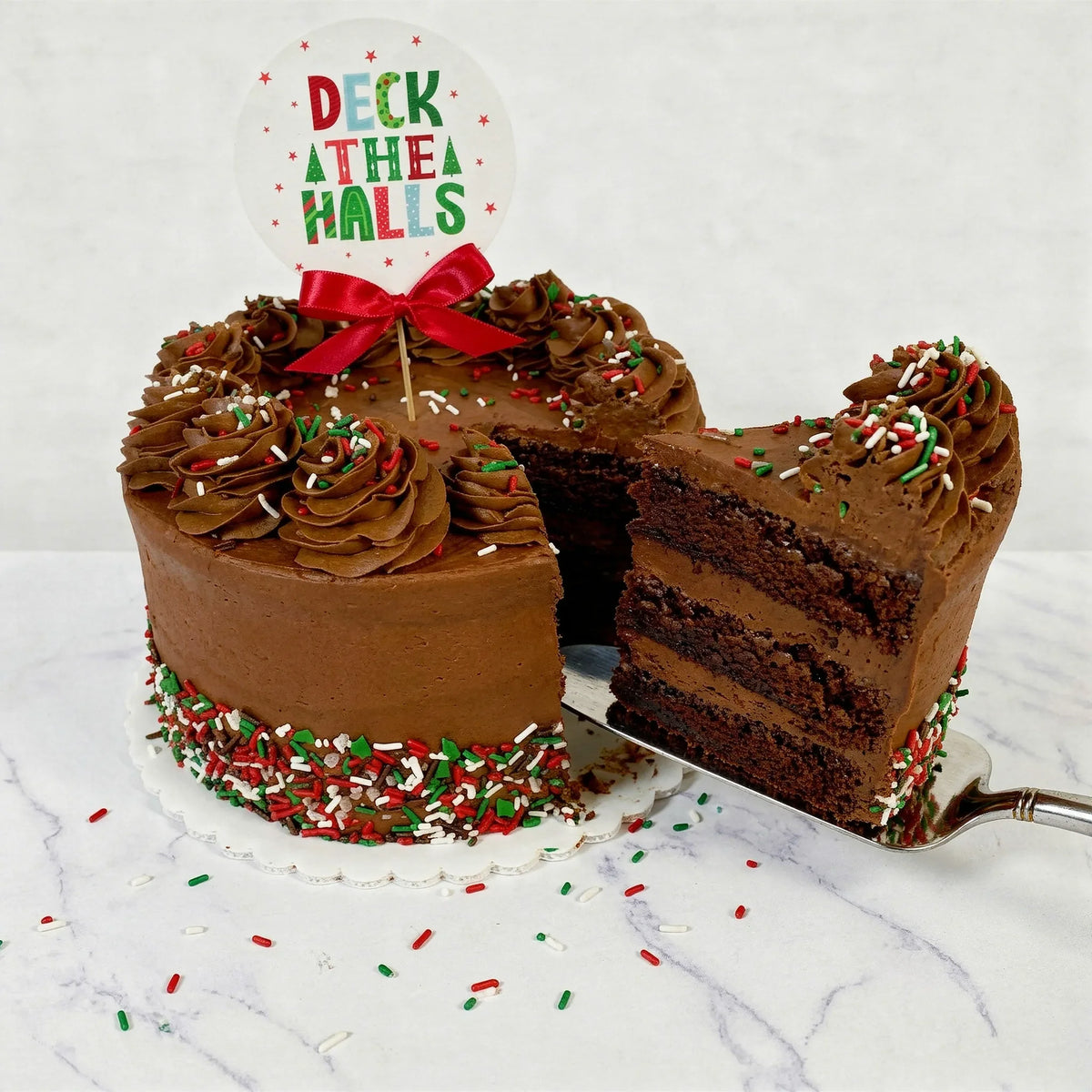 Sliced Christmas sprinkles chocolate cake showing chocolate layers and buttercream filling under a Deck the Halls topper, kosher, made in Chestnut Hill MA
