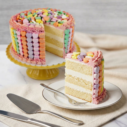 Sliced conversation heart cake showing vanilla layers with buttercream filling and pastel candy hearts on the sides, kosher, made in Chestnut Hill MA