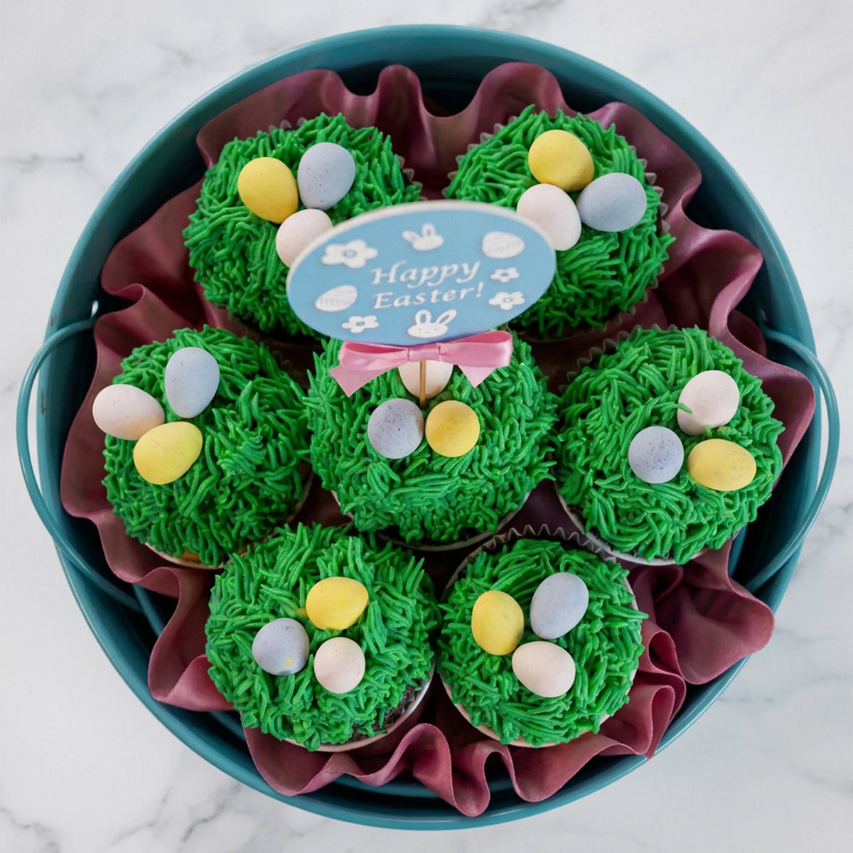 Top view of an Easter cupcake bouquet with buttercream grass and pastel candy eggs in a teal pail, kosher, made in Chestnut Hill MA