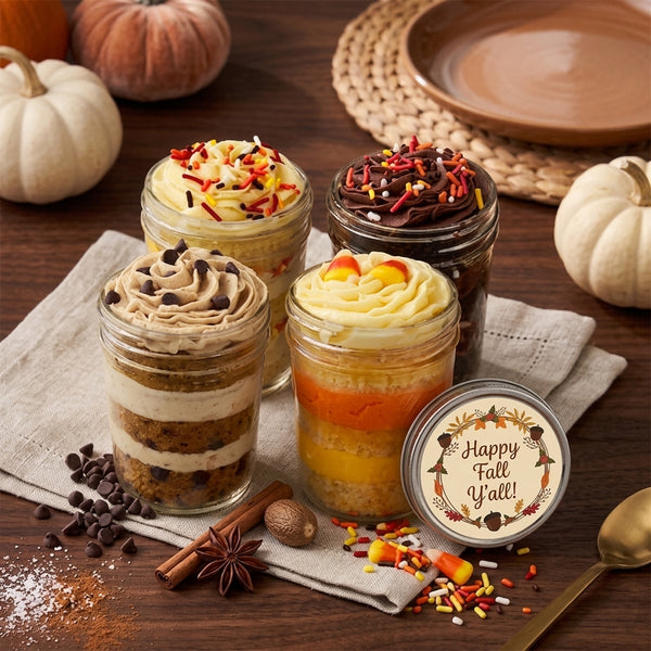 Four fall cupcake in a jar desserts with a generic Happy Fall Y'all lid, on a wood table with pumpkins.