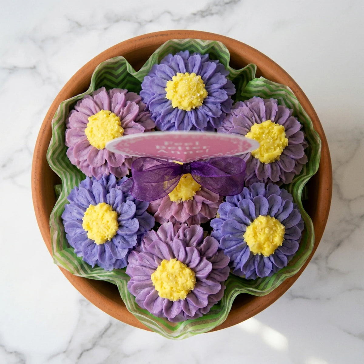 Overhead view of seven buttercream daisy cupcakes with yellow centers in a terracotta pot lined with green tissue, kosher, made in Chestnut Hill MA