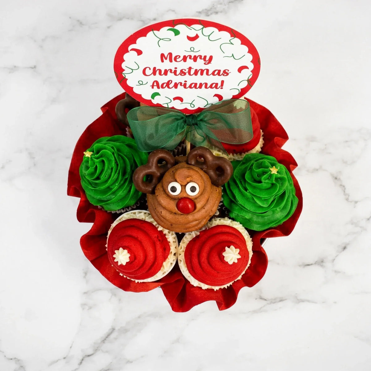 Overhead view of a Christmas cupcake bouquet with tree, Santa hat and pretzel antler reindeer cupcakes and a personalized Merry Christmas topper, kosher, made in Chestnut Hill MA