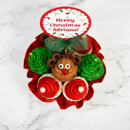 Overhead view of a Christmas cupcake bouquet with tree, Santa hat and pretzel antler reindeer cupcakes and a personalized Merry Christmas topper, kosher, made in Chestnut Hill MA