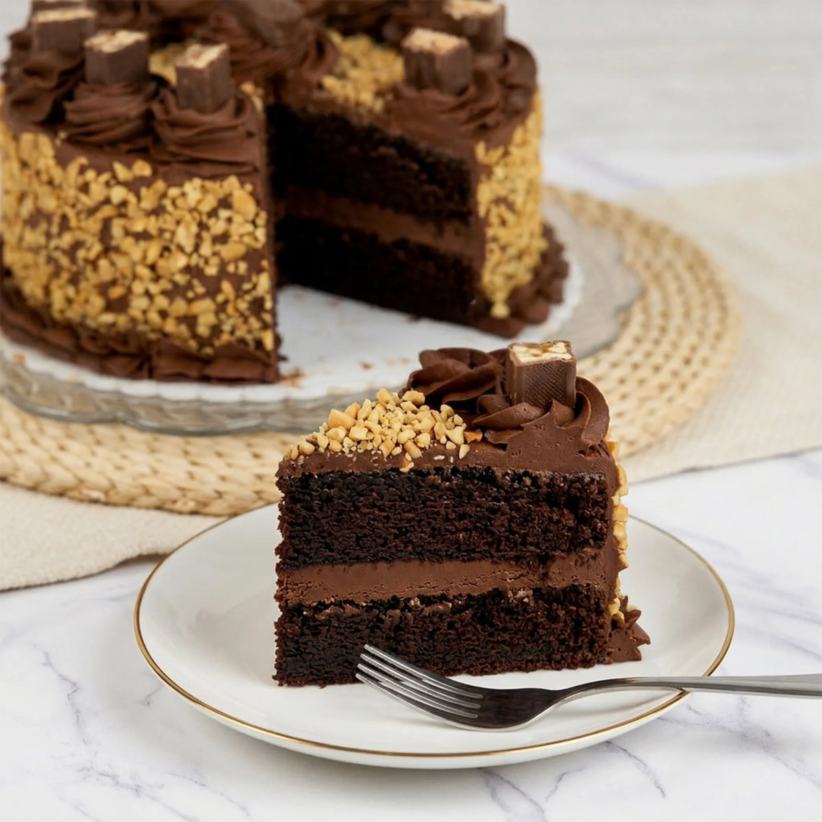 Slice of Snickers cake showing chocolate layers and chocolate buttercream filling, with the cut cake behind it, kosher, made in Chestnut Hill MA