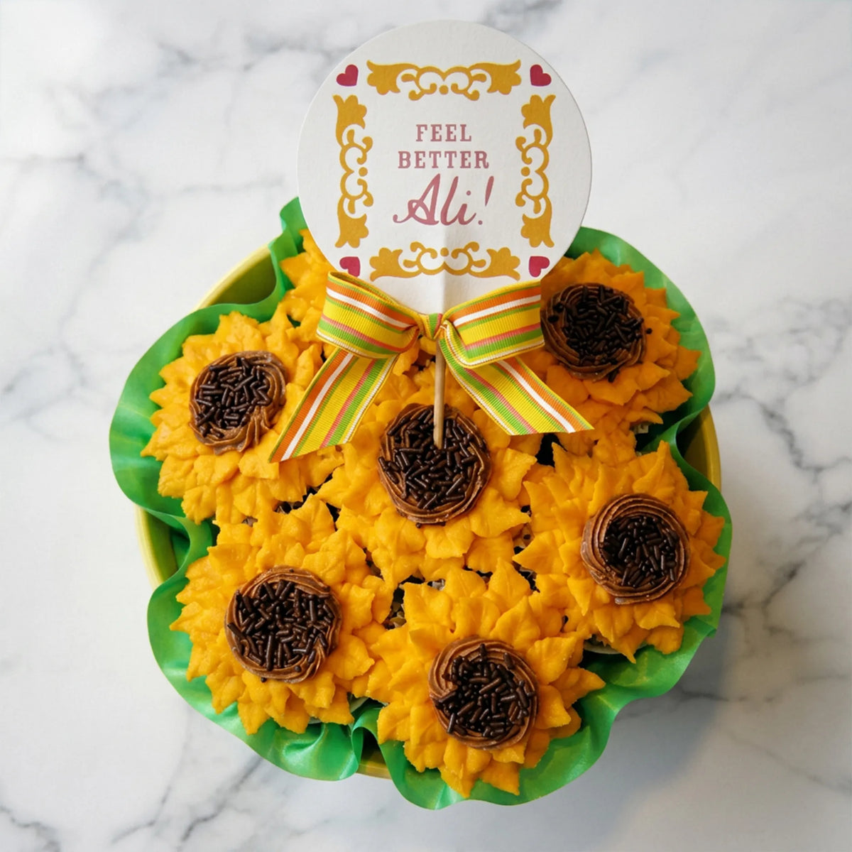 Sunflower cupcakes with golden buttercream petals and chocolate sprinkle centers on marble, one held in hand showing the vanilla cake inside, kosher, made in Chestnut Hill MA