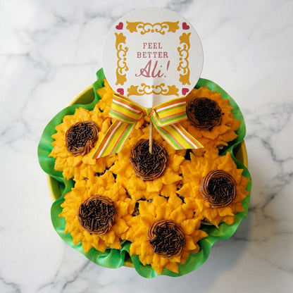 Sunflower cupcakes with golden buttercream petals and chocolate sprinkle centers on marble, one held in hand showing the vanilla cake inside, kosher, made in Chestnut Hill MA