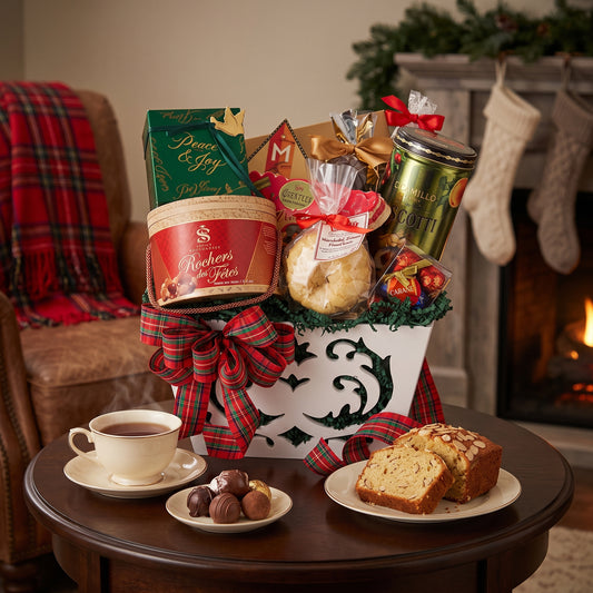 Peace and Joy holiday gift basket in a white keepsake box with tartan bow, chocolate drum and almond pound cake, on a side table beside a Christmas fireplace