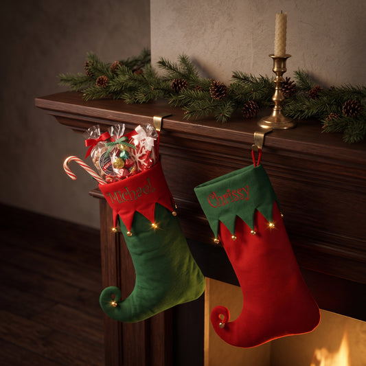 Personalized Christmas stockings in red and green felt embroidered with names, hanging from a wood mantel with spruce garland